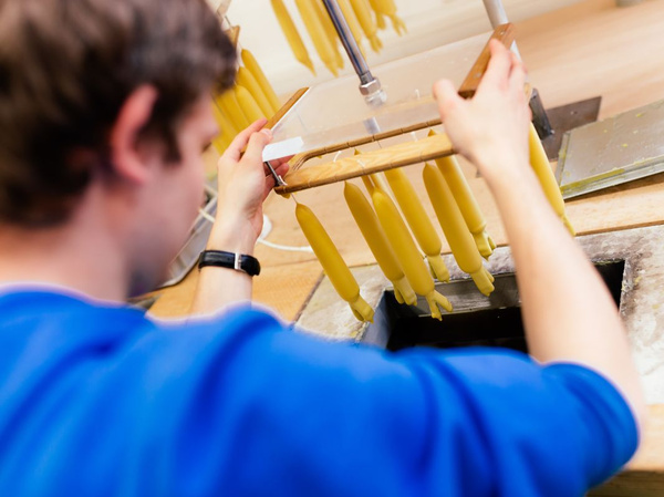 KI generiert: Eine Person taucht gelbe Kerzen in flüssiges Wachs.