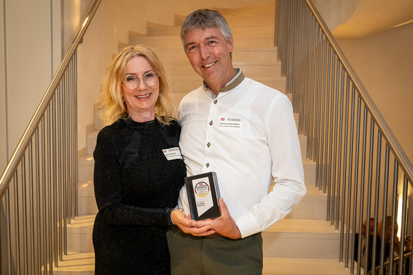 KI generiert: Das Bild zeigt ein hölzernes Brett mit einer Auswahl an verschiedenen Käsesorten, Trauben, Nüssen und Baguettescheiben. Daneben stehen zwei Weingläser, eines davon mit Rotwein gefüllt.