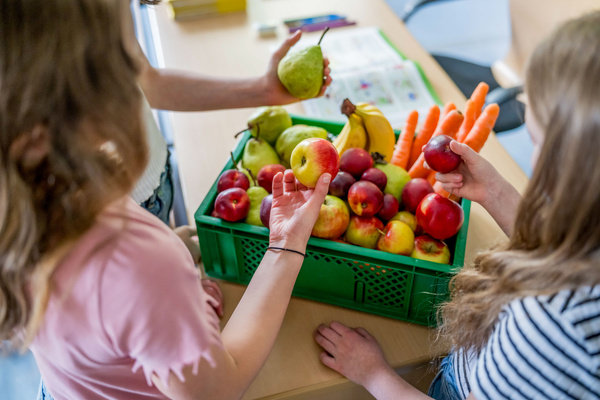 KI generiert: Zwei Kinder betrachten eine Kiste mit frischem Obst und Gemüse auf einem Tisch.