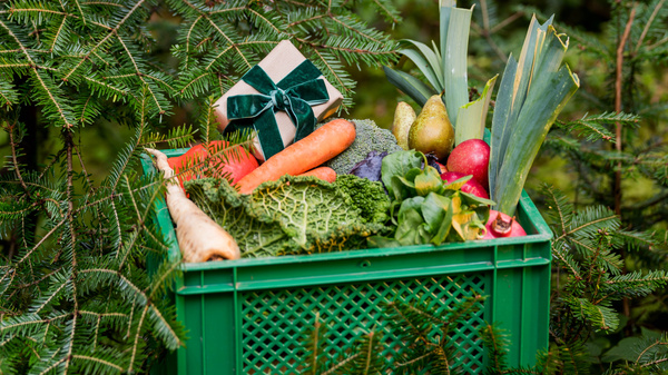 KI generiert: Grüne Kiste mit verschiedenem Gemüse und einem Geschenk im Wald.