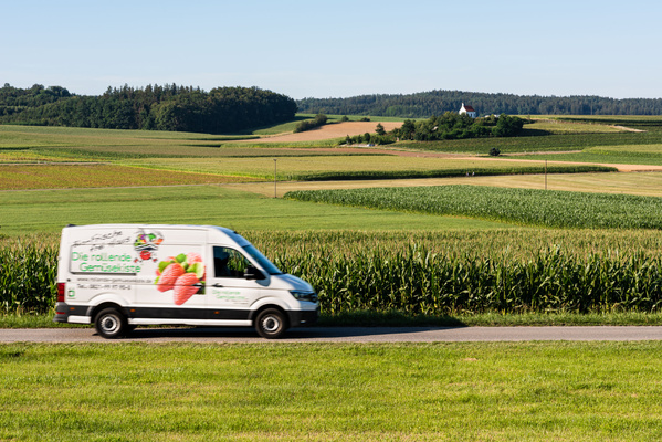 KI generiert: Ein Lieferwagen fährt an Kornfeldern vorbei. Text: "Die rollende Gemüsekiste".