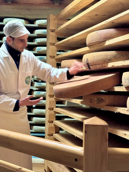 KI generiert: Ein Mann in weißer Arbeitskleidung prüft Laibe in einem Käselager.