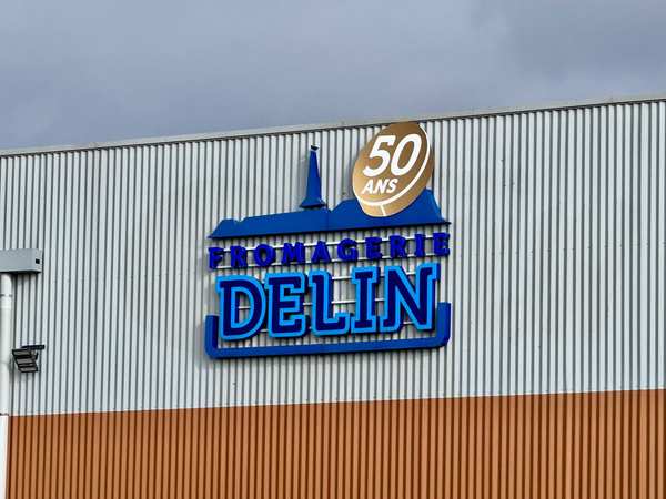 KI generiert: Gebäude mit "FROMAGERIE DELIN" und "50 ANS" Schild, grauer Himmel im Hintergrund.