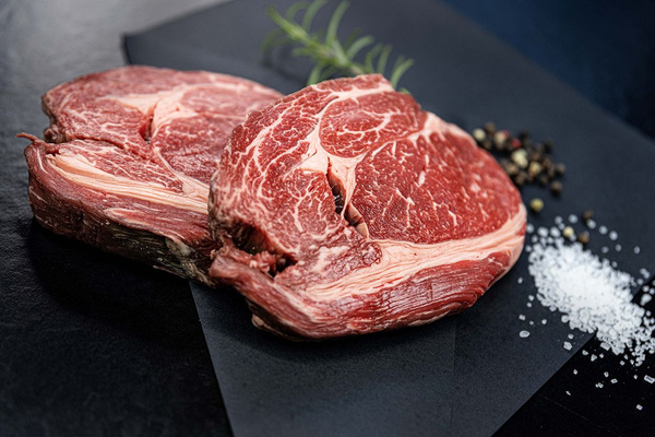 KI generiert: Das Bild zeigt zwei Personen in grüner Arbeitskleidung, die lächelnd eine Kiste mit frischem Obst und Gemüse halten. Im Hintergrund sind weitere Kisten mit Tomaten, Äpfeln und Salat zu sehen, was auf ein Lager oder eine Verkaufsstelle für frische Lebensmittel hinweist.