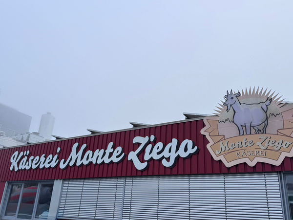 KI generiert: Gebäude der Käserei Monte Ziego mit Logo einer Ziege. Text: "Käserei Monte Ziego" und "Monte Ziego Käserei".