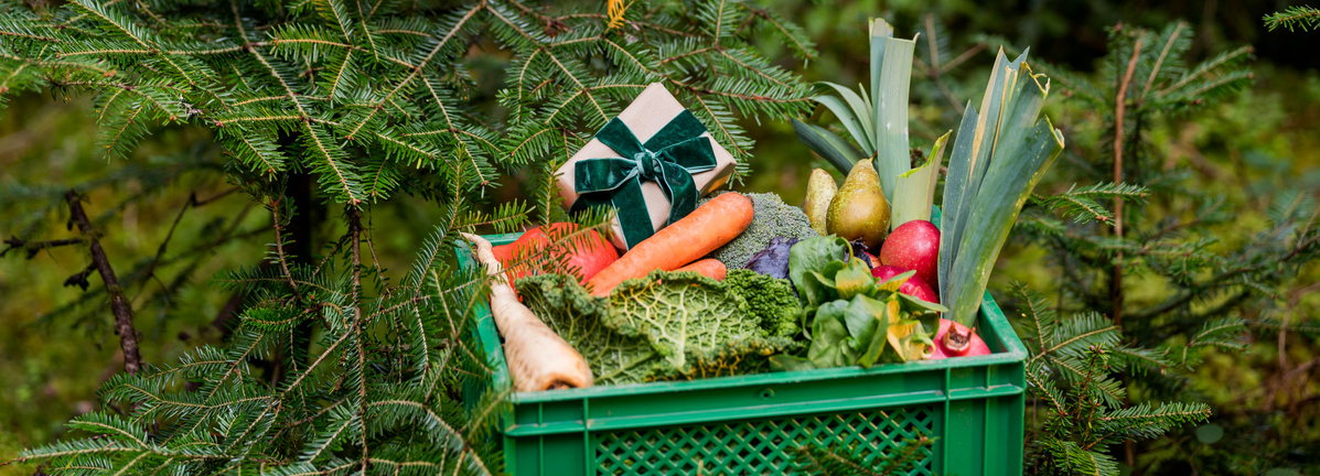 KI generiert: Eine Kiste mit Gemüse und Früchten im Wald, dekoriert mit einem Geschenk.