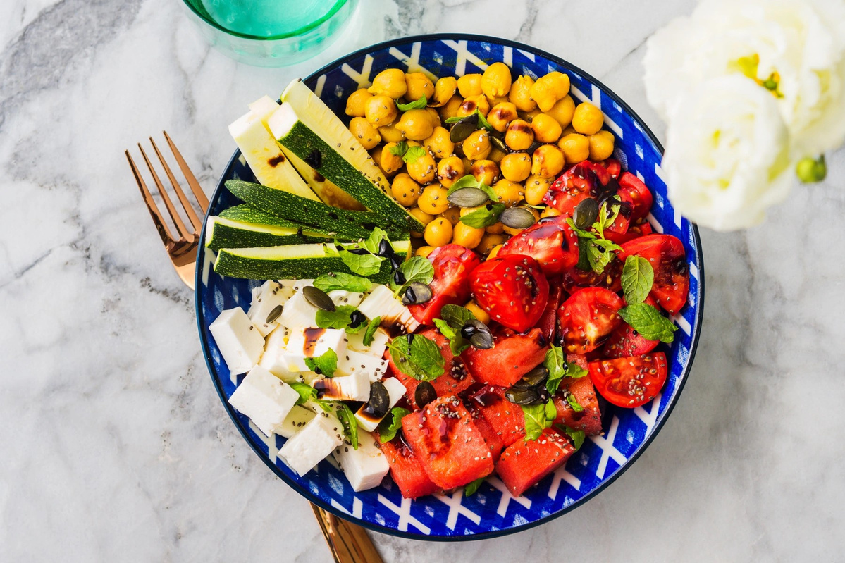 KI generiert: Das Bild zeigt eine Schüssel mit einem bunten Salat aus Rote-Bete-Scheiben, Karottenstreifen, Feldsalat, gehackten Nüssen und einem Klecks Sahne oder Joghurt in der Mitte. Der Salat liegt auf einem Holztisch.