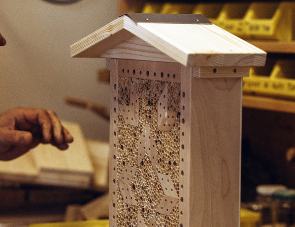 KI generiert: Ein Insektenhotel aus Holz in einer Werkstatt, eine Hand ist teilweise sichtbar.
