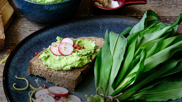 KI generiert: Brot mit Avocado-Aufstrich und Radieschen, daneben frischer Bärlauch auf einem Teller.