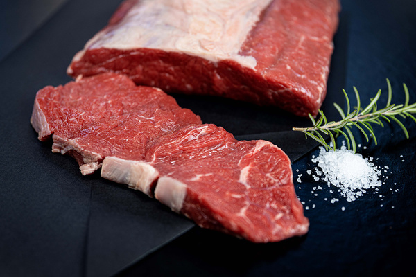 KI generiert: Das Bild zeigt zwei Personen in grüner Arbeitskleidung, die lächelnd eine Kiste mit frischem Obst und Gemüse halten. Im Hintergrund sind weitere Kisten mit Tomaten, Äpfeln und Salat zu sehen, was auf ein Lager oder eine Verkaufsstelle für frische Lebensmittel hinweist.