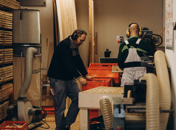 KI generiert: Zwei Männer arbeiten mit Gehörschutz in einer Holzwerkstatt mit Maschinen und Holzbrettern.