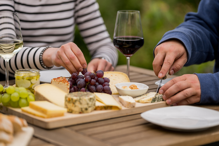 KI generiert: Zwei Personen genießen eine Käseplatte mit Wein auf einem Holztisch im Freien.