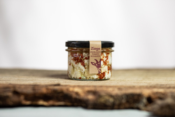 KI generiert: Ein Glas mit Ziegenkäse, Knoblauch, Tomate, Rosmarin. Text: "Ziege Knoblauch Tomate Rosmarin".