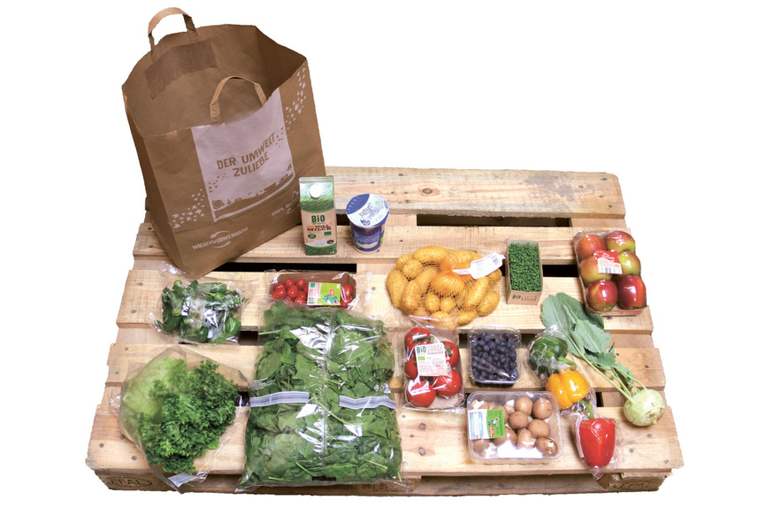 KI generiert: Eine Auswahl an Bio-Lebensmitteln auf einer Holzpalette mit einer Papiertüte. Text auf der Tüte: "DER UMWELT ZULIEBE".