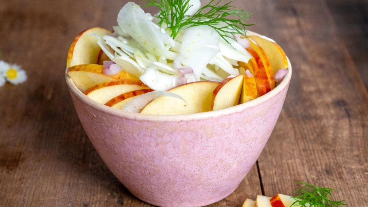 KI generiert: Das Bild zeigt eine Schüssel mit einem bunten Salat aus Rote-Bete-Scheiben, Karottenstreifen, Feldsalat, gehackten Nüssen und einem Klecks Sahne oder Joghurt in der Mitte. Der Salat liegt auf einem Holztisch.