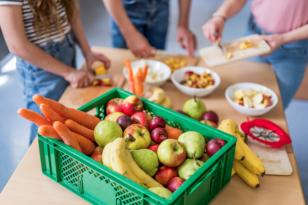 KI generiert: Eine grüne Kiste voller Obst und Gemüse, daneben werden Früchte geschnitten.