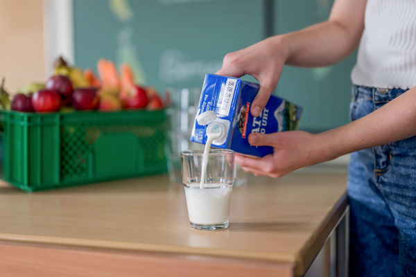KI generiert: Eine Person gießt Milch aus einer Verpackung in ein Glas.