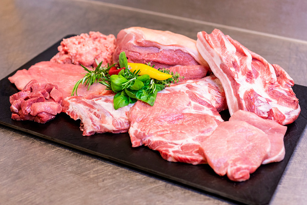 KI generiert: Verschiedene Schweinefleischstücke auf einem Tablett, dekoriert mit frischen Kräutern und Chili.