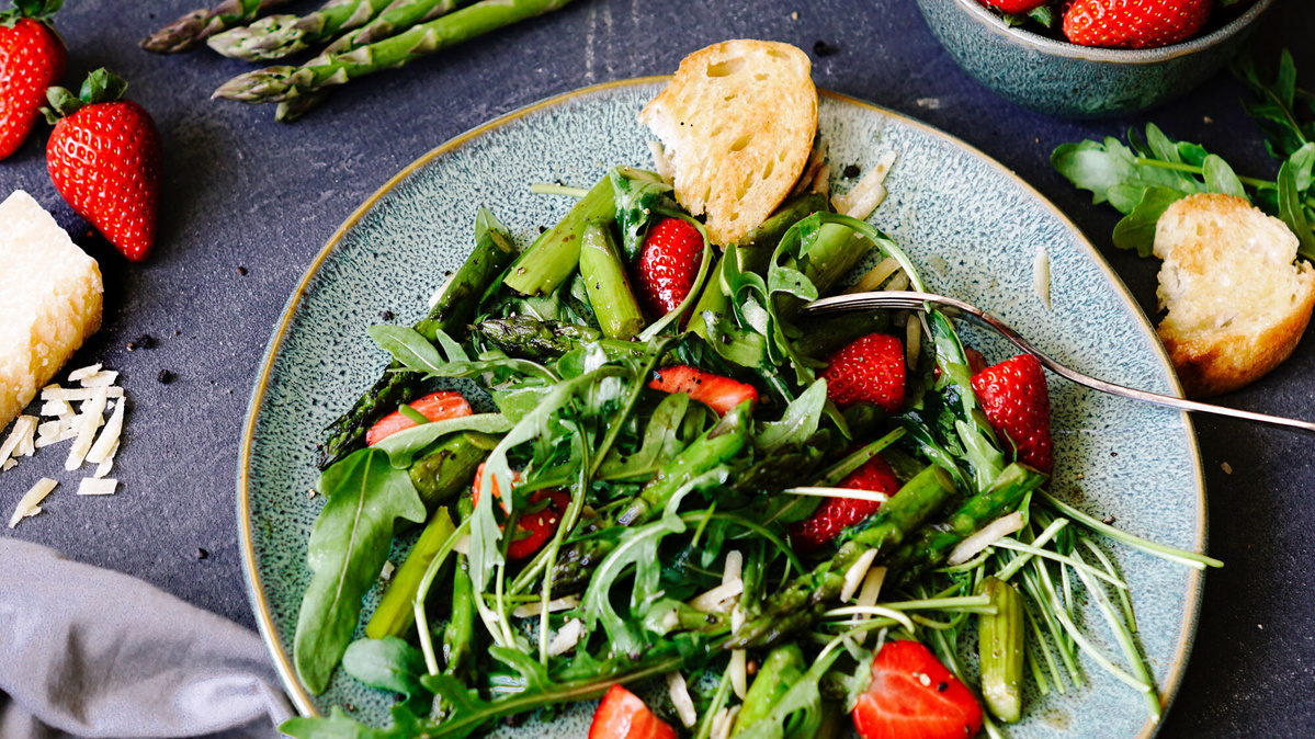 KI generiert: Das Bild zeigt eine Schüssel mit einem bunten Salat aus Rote-Bete-Scheiben, Karottenstreifen, Feldsalat, gehackten Nüssen und einem Klecks Sahne oder Joghurt in der Mitte. Der Salat liegt auf einem Holztisch.