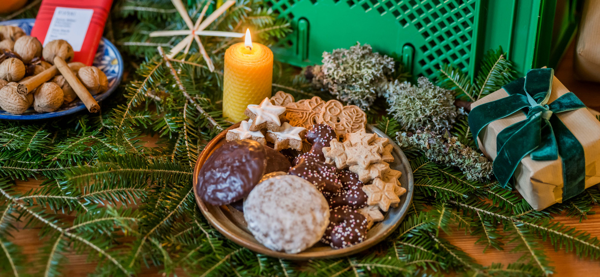 KI generiert: Weihnachtliches Stillleben mit Keksen, Kerze, Nüssen und Geschenk auf Tannenzweigen.