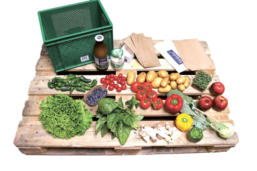 KI generiert: Eine bunte Auswahl an frischem Gemüse und Obst auf einer Palette, neben einer leeren grünen Kiste.